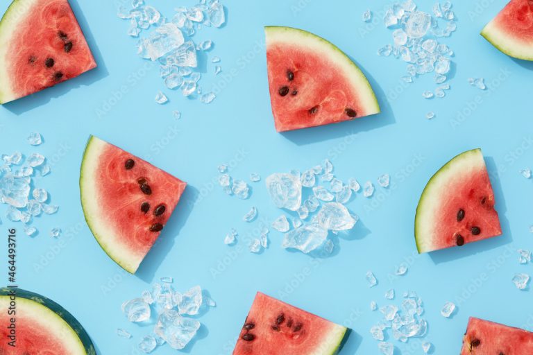 Summer creative wallpaper. Watermelon pattern with sunlight. Sliced fruit with ice on blue background